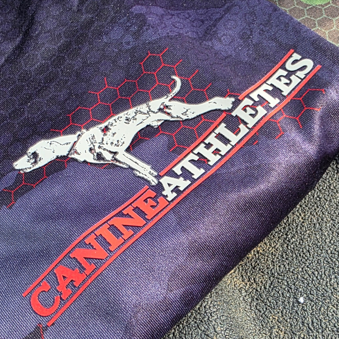 Folded black camo shirt with 'Canine Athletes' text and dog illustration on a textured surface