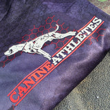 Folded black camo shirt with 'Canine Athletes' text and dog illustration on a textured surface