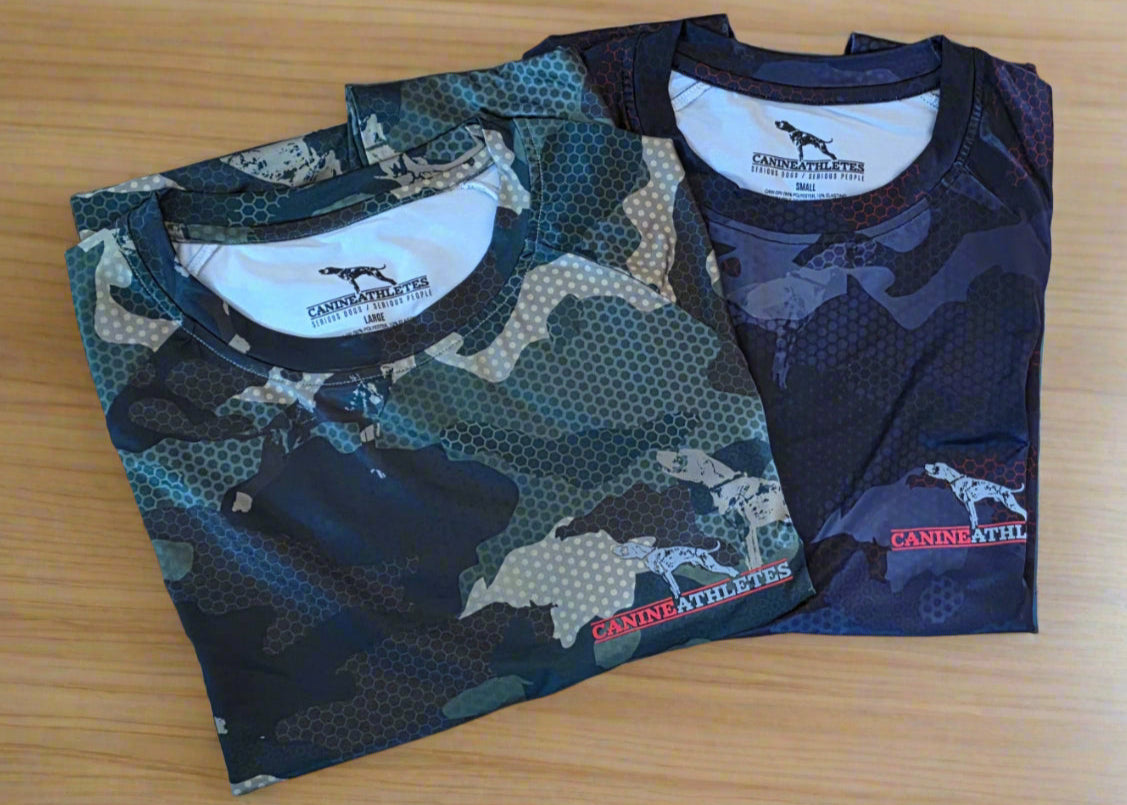 Two camouflage-patterned canine athletes shirts on a wooden floor