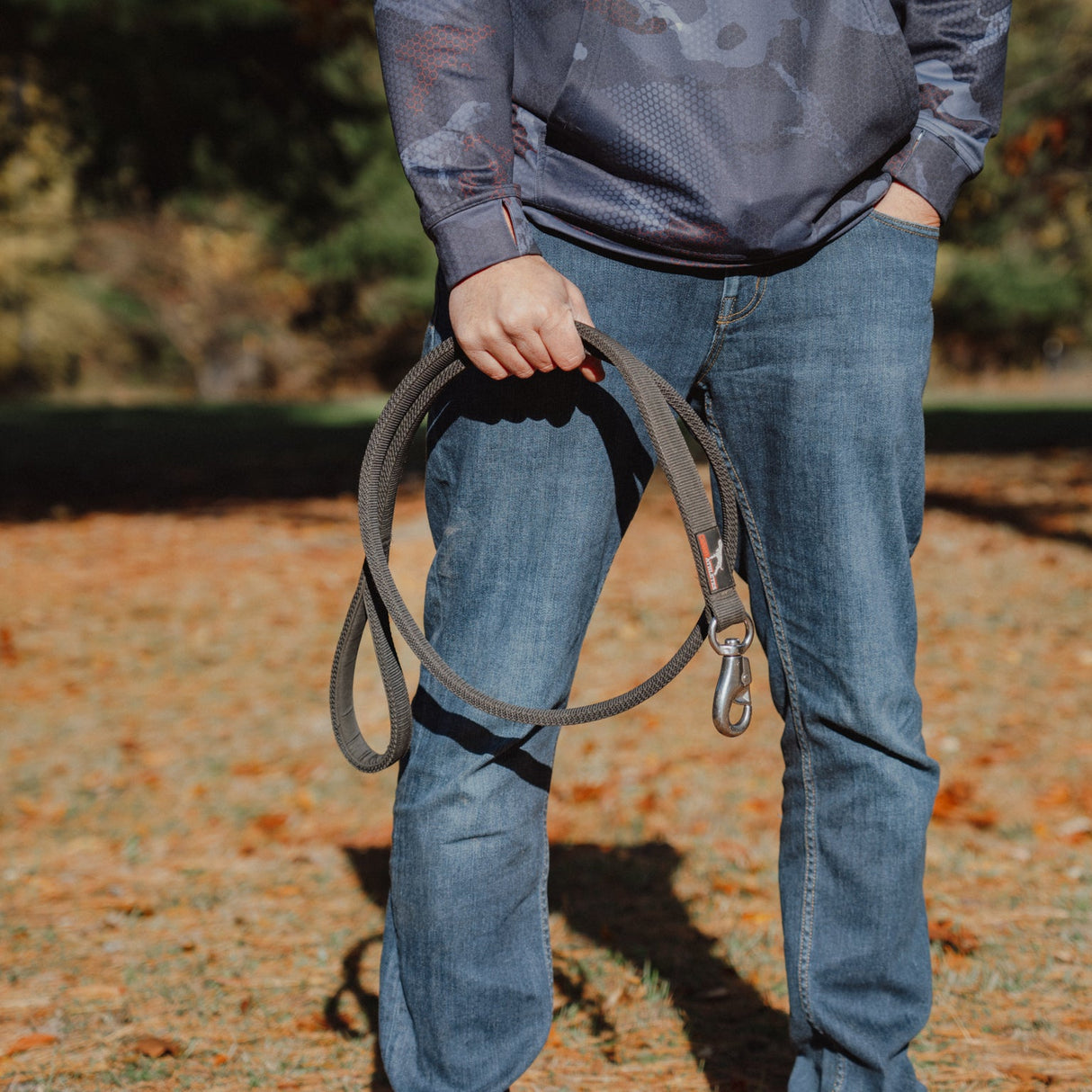 Person holding a dog leash outdoors on a grassy area with trees in the background