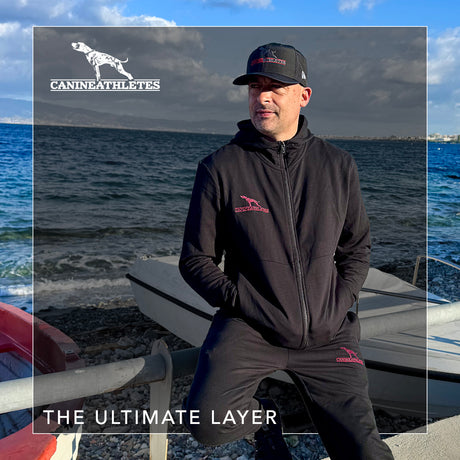 Man wearing a branded jacket and cap by the water with 'Canine Athletes' branding.